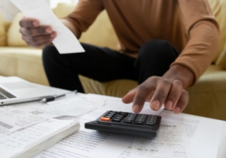 a man looks at a coffee table covered with receipts and a calculator