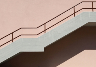 Concrete staircase with brown metallic railing on pink painted facade