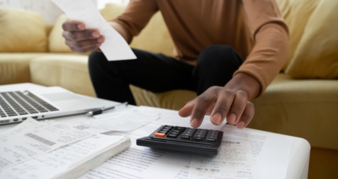 a man looks at a coffee table covered with receipts and a calculator