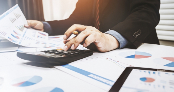 man in business suit with calculator surrounded by graphs and paperwork