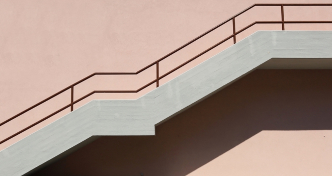 Concrete staircase with brown metallic railing on pink painted facade